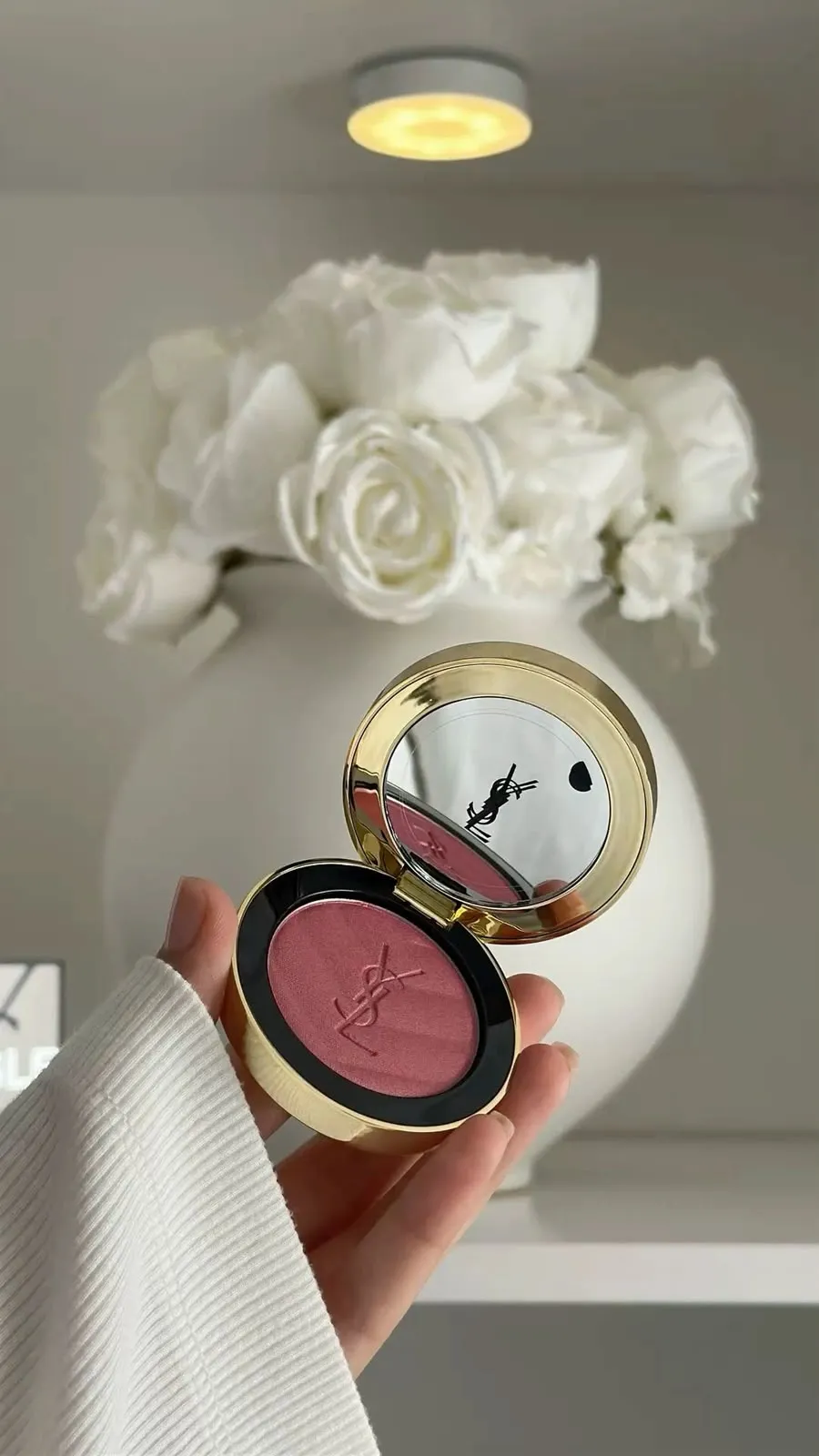 Luxury blush compact held before white roses